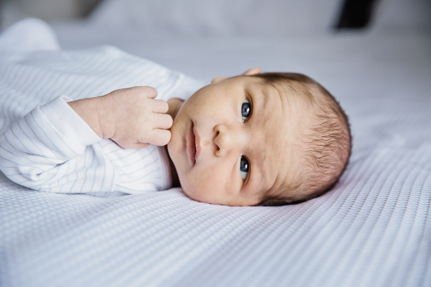 newborn-baby-looking-at-camera-with-hand-to-mouth-Natural-family-photography